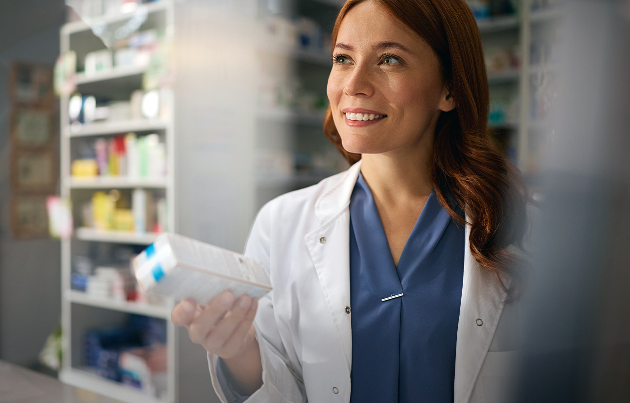 Apothekerin hält lächelnd ein Medikament in der Hand